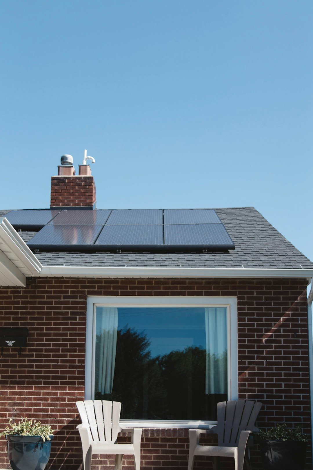 Why Residential Solar Energy Is a Smart Long-Term Investment Vivint Solar - Solar Panels on roof of brick home with window and Adirondack chairs.